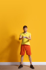 Happy smiling. Young caucasian man using smartphone, serfing, chatting, betting. Full length portrait isolated on yellow background. Concept of modern technologies, millennials, social media.