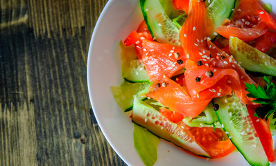 Salad with smoked salmon and cucumber, tomato, pepper in bowl on a wooden background