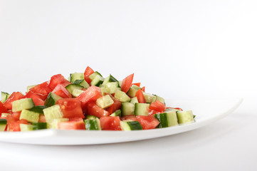 Tomato and cucumber salad on a white plate. Diced raw vegetables. Close-up. Isolate
