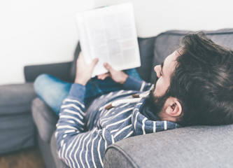 man relaxing on couch while reading magazine or newspaper