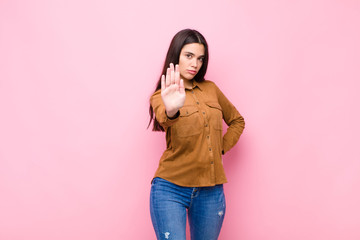 young pretty woman looking serious, stern, displeased and angry showing open palm making stop...