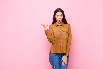 young pretty woman looking astonished in disbelief, pointing at object on the side and saying wow,...
