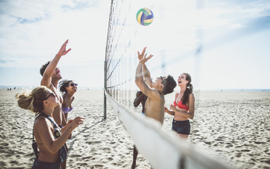 Group of friends playing beach volley on the beach and having fun