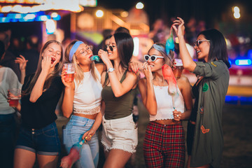 Female friends eating cotton candy and drinking beer in amusement park