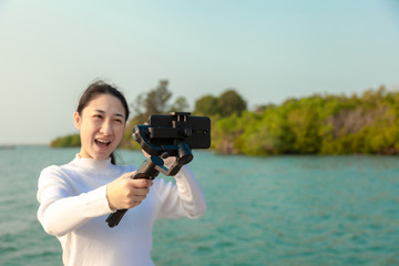 Blogger Asian woman record vlog video and sharing content on streaming platform with Social Network. female enjoy in front of camera using mobile phone make vlogging live feeds on social media network