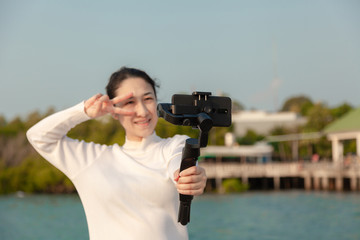 Blogger Asian woman record vlog video and sharing content on streaming platform with Social Network. female enjoy in front of camera using mobile phone make vlogging live feeds on social media network