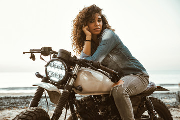 Fototapeta na wymiar Beautiful girl having fun driving her custom cafe racer motorcycle, enjoying the sunset on the beach