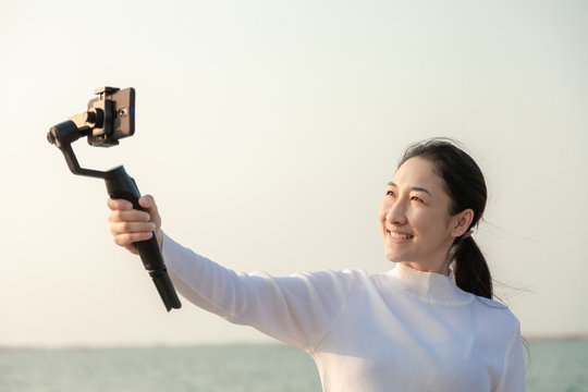 Blogger Asian woman record vlog video and sharing content on streaming platform with Social Network. female enjoy in front of camera using mobile phone make vlogging live feeds on social media network
