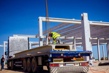 Worker is attaching crane hooks to concrete joist in truck trailer