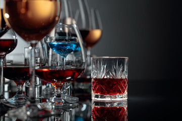 Set of various alcoholic beverages in glasses on a black reflective background.