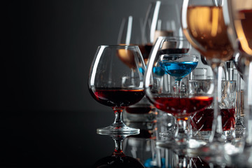 Set of various alcoholic beverages in glasses on a black reflective background.