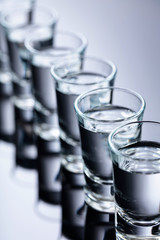 Glasses of vodka on a black reflective background.