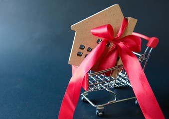 Wood model houses tied with red ribbon in small cart supermarket on black background. Show to...