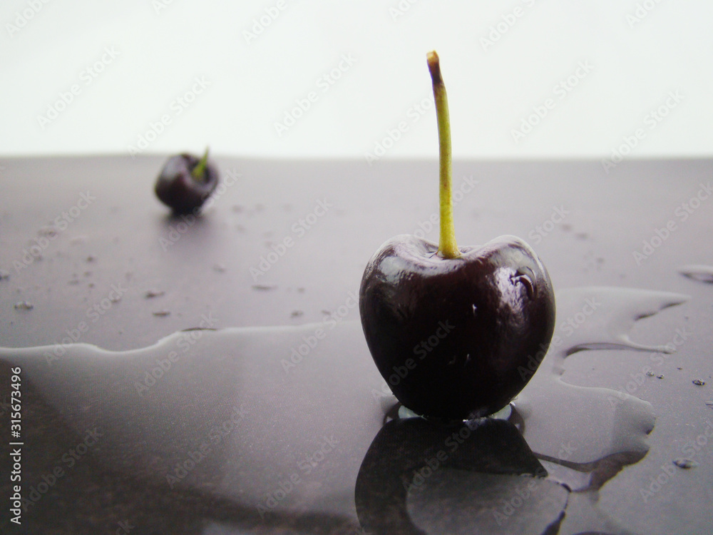 Wall mural a pool of water.fresh black cherries lined up on a black gray background