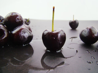 A pool of water.Fresh black cherries lined up on a black gray background