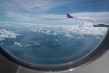 Naklejka na ściany i meble Wing of airplane flying above Hong Kong city background through the window.