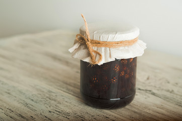 Traditional Trend Siberian dessert - young pine cones jam. Ukrainian cone jam in a jar on a light background close-up and copy space.