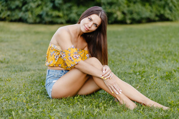 Naklejka na ściany i meble Cute girl in denim shorts sitting on the grass in the park