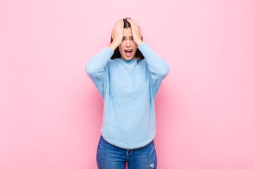 young pretty woman feeling horrified and shocked, raising hands to head and panicking at a mistake...