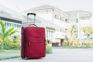A large red suitcase stands on the street of the hotel against the background of houses and...