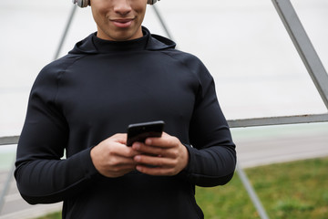Photo of athletic smiling sportsman using headphones and cellphone
