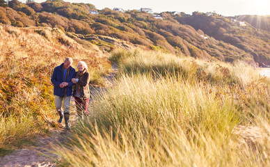 Fototapeta premium Loving Active Senior Couple Arm In Arm Walking Through Sand Dunes
