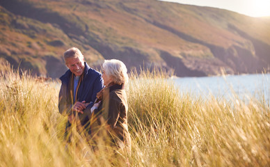 Loving Active Senior Couple Arm In Arm Walking Through Sand Dunes