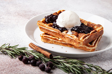 Belgian waffles with ice cream on a white plate and rosemary berry jam. Waffer with jam and icecream on craft background.