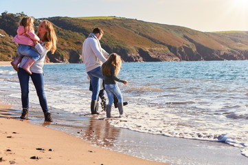 Family Playing On Beach Jumping Over Waves Looking Out To Sea