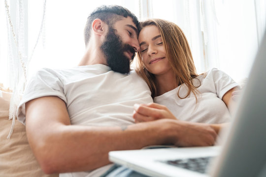 Image of romantic calm couple using laptop and hugging while sitting