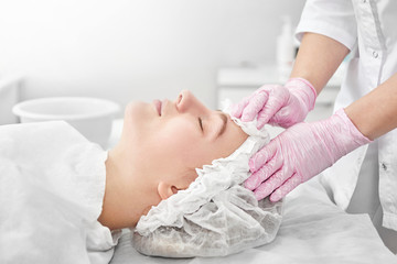 Obraz na płótnie Canvas Professional beautician in salon provides comprehensive facial skin care for young woman. Pore cleansing procedures, all-season peeling, firming anti-aging mask