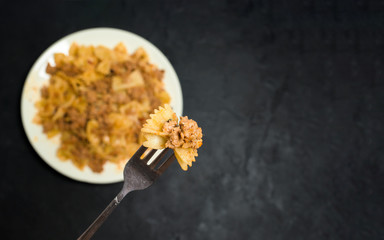 Obraz na płótnie Canvas pasta with meat on a dark background. on a fork, pasta in the shape of a butterfly with meat . the view from the top. space for text. photo for banner