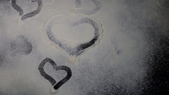 Flour is sprinkled on the table. They draw a heart on it with a finger. Valentine's Day. Dark marbled background. White flour.
