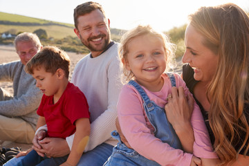 Family With Grandfather Relaxing On Beach With Flaring Sun