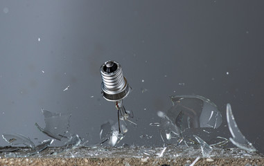 a falling round incandescent lamp is broken into fragments on a stone on a gray background
