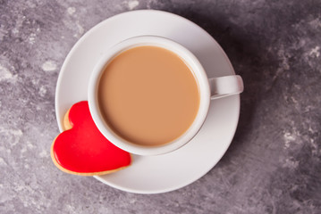 Cup of coffee and a heart shaped red cookie on the gray table.