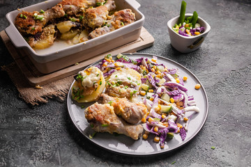 Appetizing baked chicken legs with potatoes, cheese and red salad.