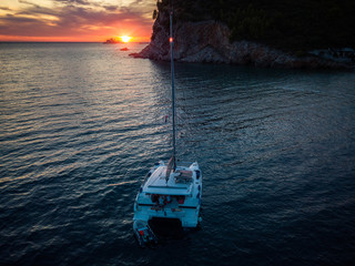 Fototapeta na wymiar Aerial view of a cliff overlooking the sea and a catamaran moored at sunset, boat. Buljarica Beach. In the background Katic Island, Petrovac, Montenegro. 