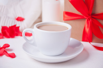 Cup of coffee and a heart shaped red cookie with gift box on the white table