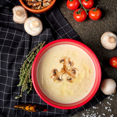 Bowl of mushroom cream soup with fried champignon mushrooms and vegetables on black stone background. Rustic style. Close up.