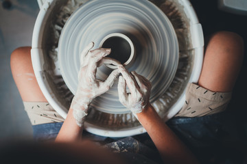 Top view of female potter's hands working on pottery wheels with eco friendly clay makes mug, concept for workshop and master class, Handcraft Ceramic Art People  - obrazy, fototapety, plakaty