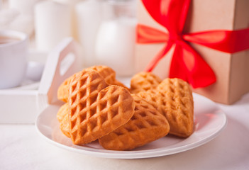 Cup of coffee and a heart shaped cookies on the white plate with gift box on the white table