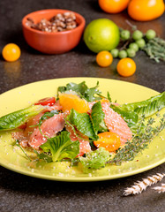 Cold salmon salad with green leaves, cucumber, avocado, lime and tomato on black stone background. Top view with copy space. Rustic style.