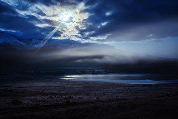 The predawn fog over the Dzhangyskol lake in the tract Eshtykol and the North Chuysky ridge in the moonlight. Russia, Altai Republic