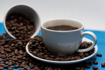 Coffee cup put on blue wooden table with spread coffee bean.