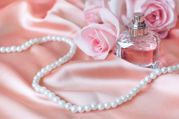 Female perfume bottle, rose, pearls on pink silk.