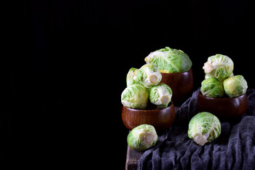 Raw brussels sprouts in wooden cups against the black background