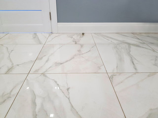 Marble floor. Square glossy tile with patterns, part of the wall and plastic baseboard