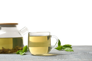 Cup of green tea, pot and leaves on grey wooden table