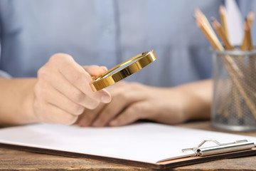 Woman using magnifying glass at table, closeup